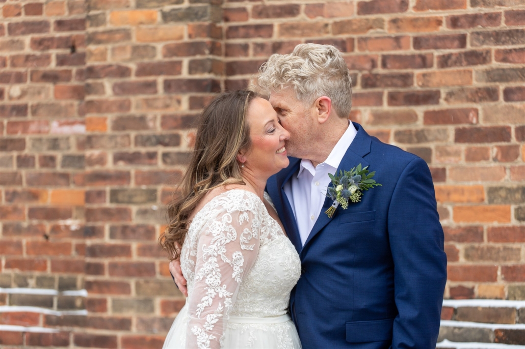 bride and groom in front of brick wall
