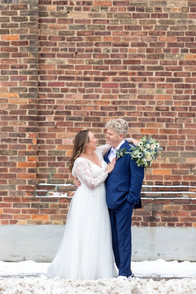 bride and groom in front of brick wall