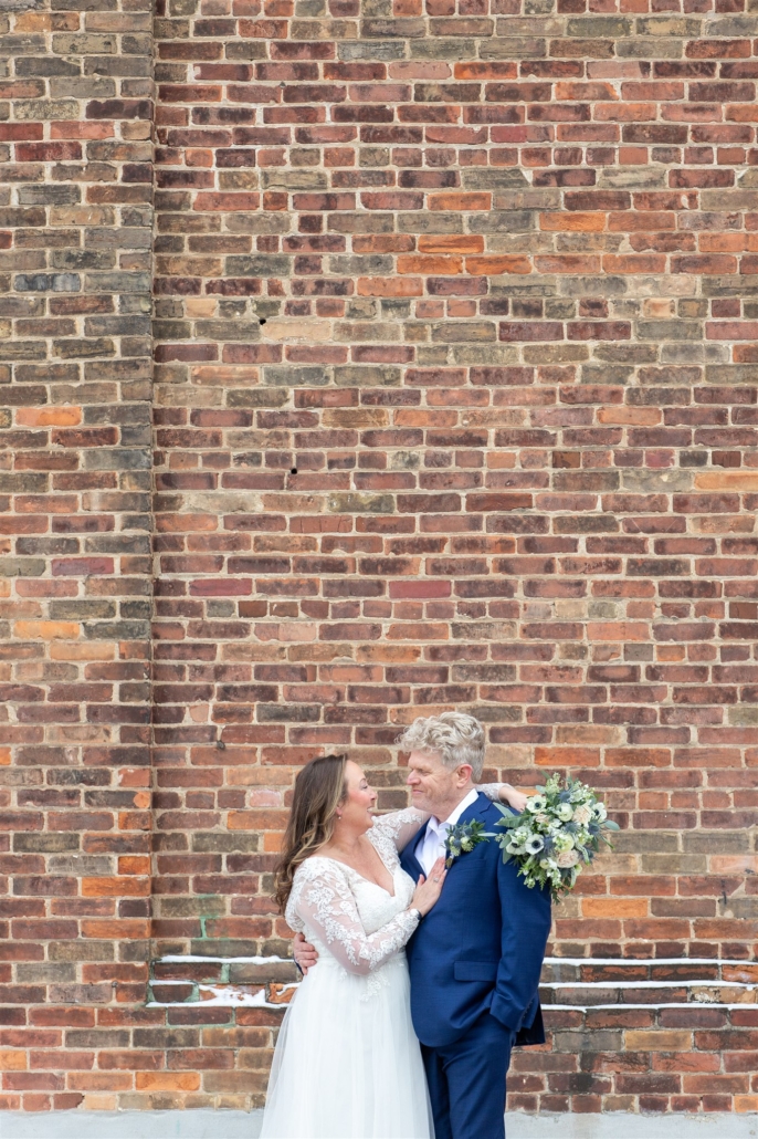 bride and groom in front of brick wall